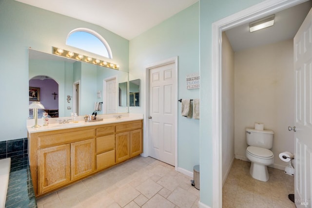 ensuite bathroom with toilet, double vanity, baseboards, and a sink