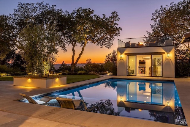 pool at dusk with a patio and an outdoor pool