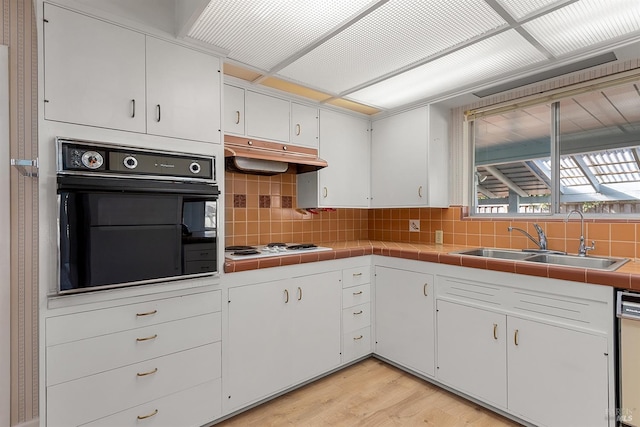 kitchen with sink, white cabinetry, light wood-type flooring, tile counters, and white appliances