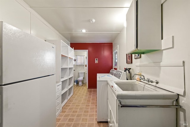 kitchen featuring sink, washing machine and clothes dryer, white cabinets, and white fridge