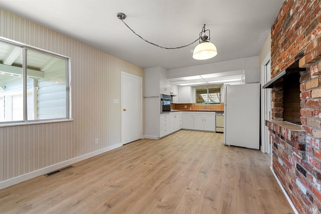 kitchen with sink, white appliances, hanging light fixtures, white cabinets, and light wood-type flooring