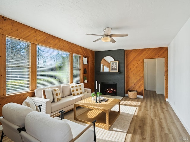 living room with a fireplace, wood walls, ceiling fan, a textured ceiling, and light hardwood / wood-style flooring