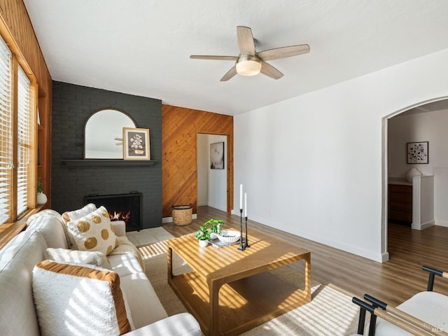 living room with ceiling fan, hardwood / wood-style floors, a brick fireplace, and wood walls