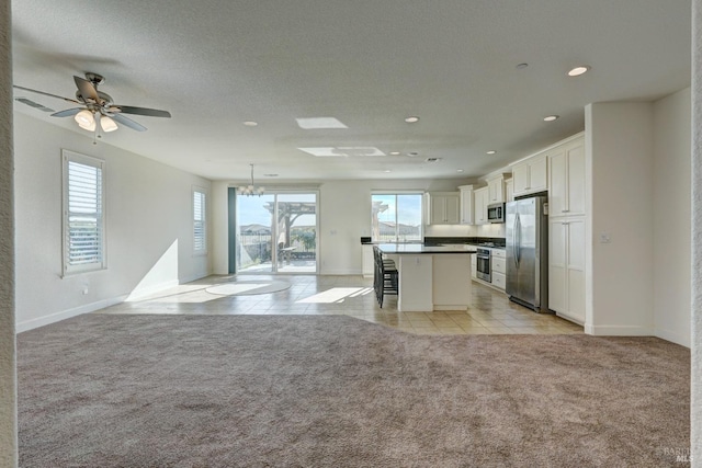 kitchen featuring appliances with stainless steel finishes, a kitchen island, white cabinets, a kitchen bar, and light colored carpet