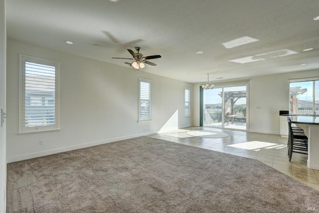 unfurnished living room with ceiling fan with notable chandelier, a healthy amount of sunlight, and light carpet