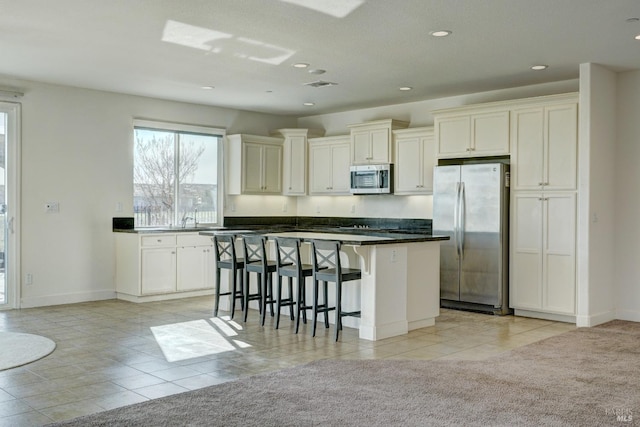 kitchen with light carpet, a kitchen breakfast bar, a kitchen island, stainless steel appliances, and white cabinets