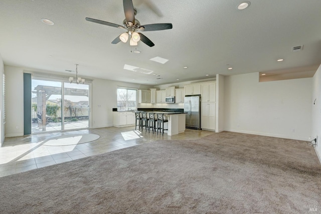 unfurnished living room featuring ceiling fan with notable chandelier and light colored carpet