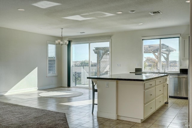 kitchen with a breakfast bar area, a center island, stainless steel dishwasher, pendant lighting, and dark stone counters