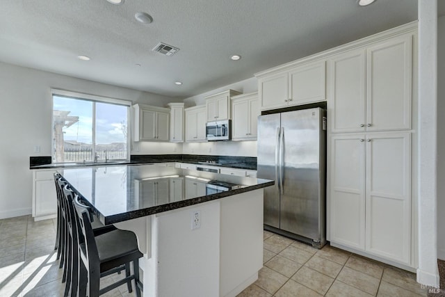 kitchen with a kitchen island, white cabinetry, appliances with stainless steel finishes, and light tile patterned floors