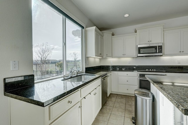 kitchen with sink, white cabinetry, light tile patterned floors, dark stone countertops, and stainless steel appliances