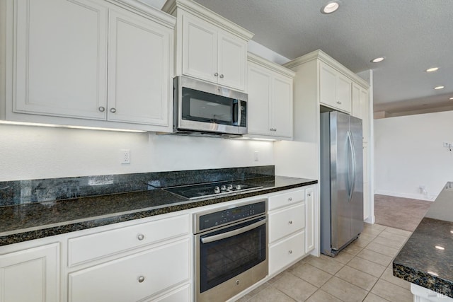 kitchen featuring light tile patterned floors, appliances with stainless steel finishes, a textured ceiling, white cabinets, and dark stone counters