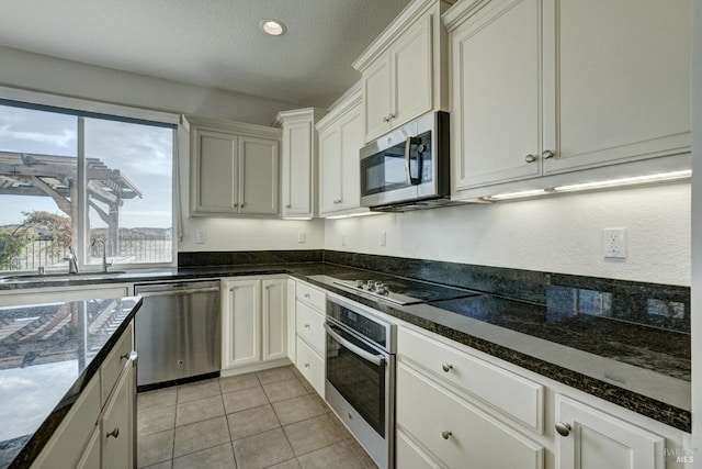 kitchen with light tile patterned floors, sink, white cabinetry, dark stone countertops, and stainless steel appliances