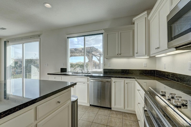 kitchen with stainless steel appliances, white cabinetry, sink, and dark stone countertops