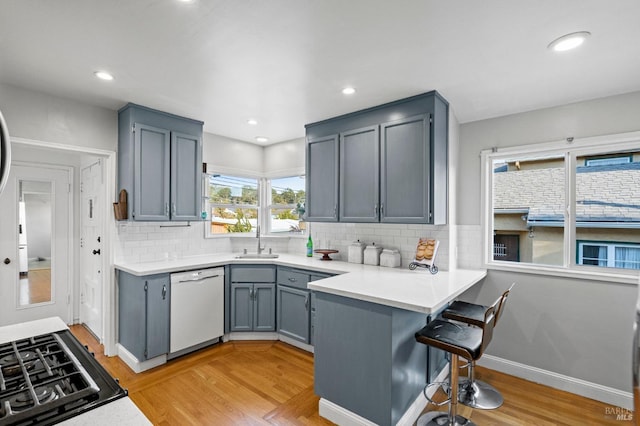 kitchen with sink, white dishwasher, kitchen peninsula, cooktop, and light hardwood / wood-style flooring