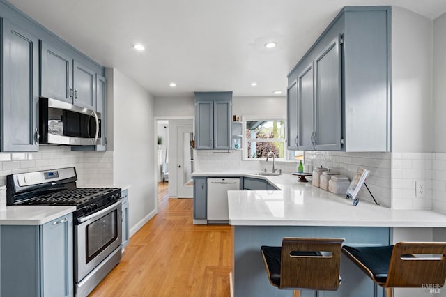 kitchen featuring appliances with stainless steel finishes, a breakfast bar, sink, kitchen peninsula, and light hardwood / wood-style flooring