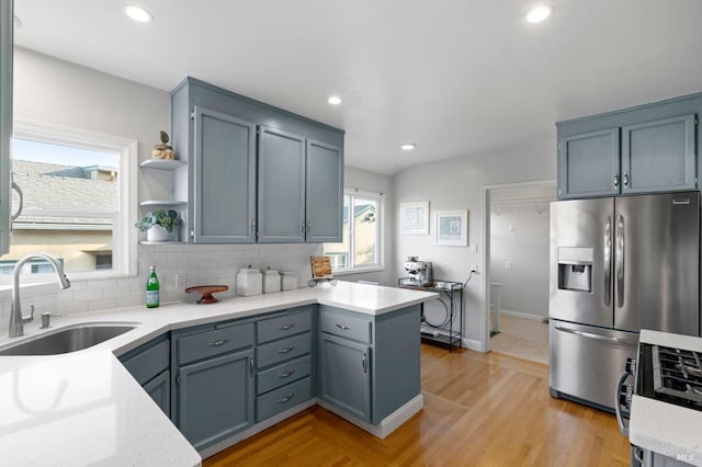 kitchen with sink, light hardwood / wood-style flooring, appliances with stainless steel finishes, decorative backsplash, and kitchen peninsula