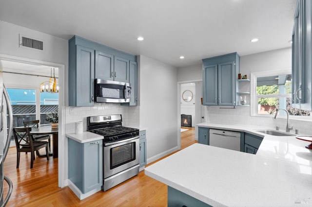 kitchen featuring sink, tasteful backsplash, light hardwood / wood-style flooring, kitchen peninsula, and stainless steel appliances