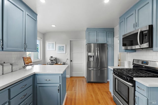 kitchen with blue cabinets, appliances with stainless steel finishes, decorative backsplash, and light hardwood / wood-style flooring