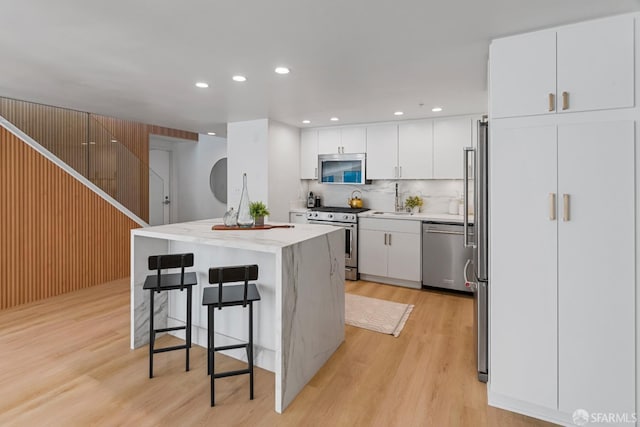 kitchen featuring a breakfast bar area, stainless steel appliances, white cabinetry, light wood-type flooring, and a center island