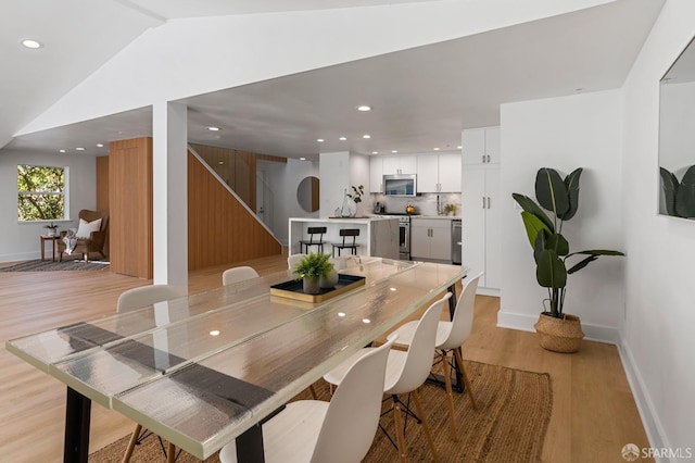 dining room featuring light wood-style flooring, baseboards, vaulted ceiling, and recessed lighting