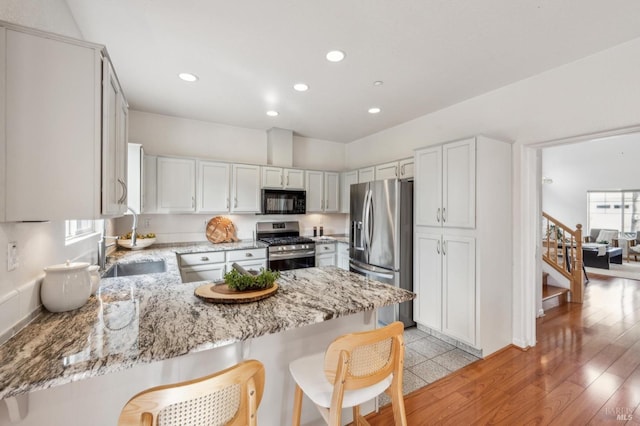 kitchen with white cabinetry, appliances with stainless steel finishes, kitchen peninsula, and a breakfast bar area