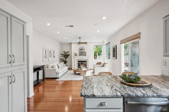 kitchen with gray cabinetry, light stone countertops, dishwasher, and light wood-type flooring