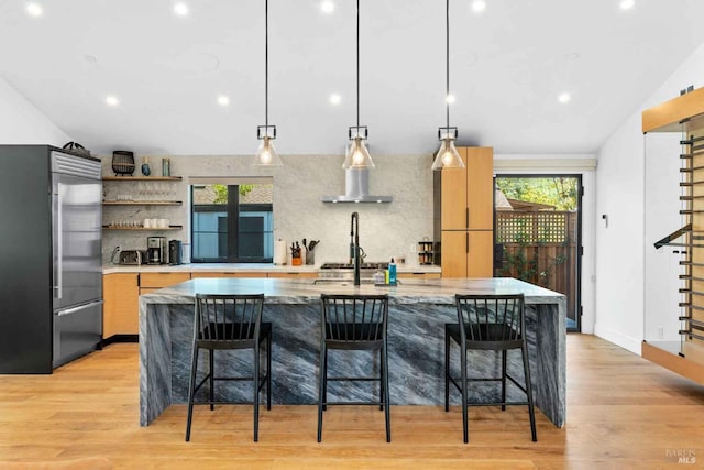 kitchen with high end fridge, pendant lighting, light hardwood / wood-style floors, and a kitchen bar