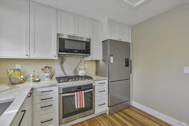 kitchen featuring backsplash, white cabinets, light stone counters, stainless steel appliances, and light wood-type flooring