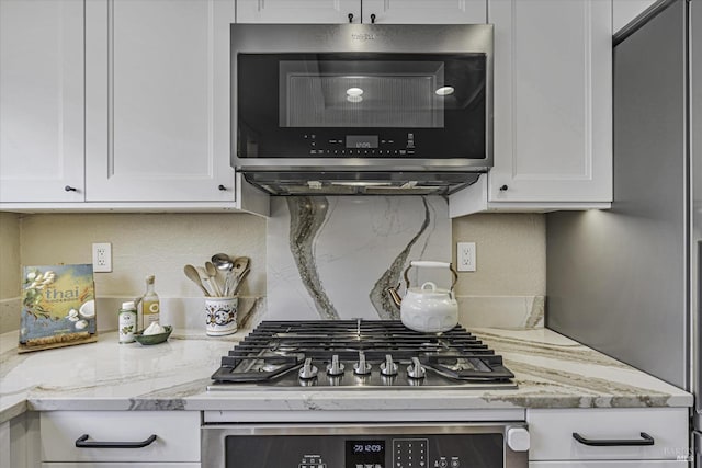 kitchen with white cabinetry, appliances with stainless steel finishes, light stone countertops, and decorative backsplash