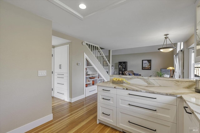 kitchen featuring white cabinetry, decorative light fixtures, light stone counters, and light hardwood / wood-style flooring