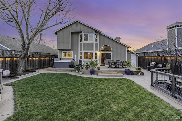 back house at dusk featuring a yard, a hot tub, and a patio area