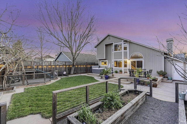 back house at dusk featuring a yard, a hot tub, and a patio