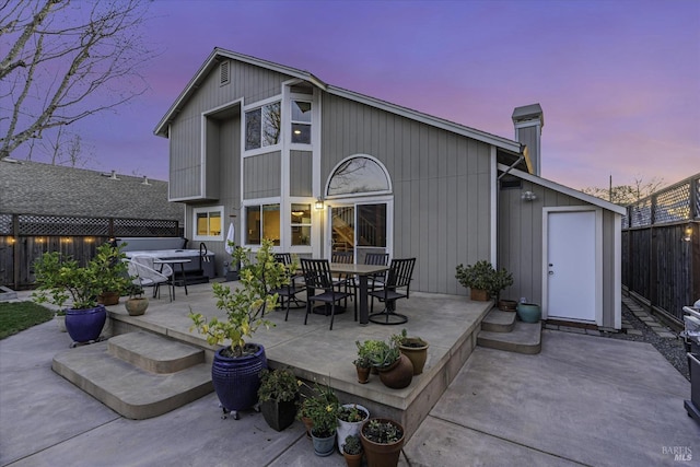 back house at dusk with a hot tub and a patio