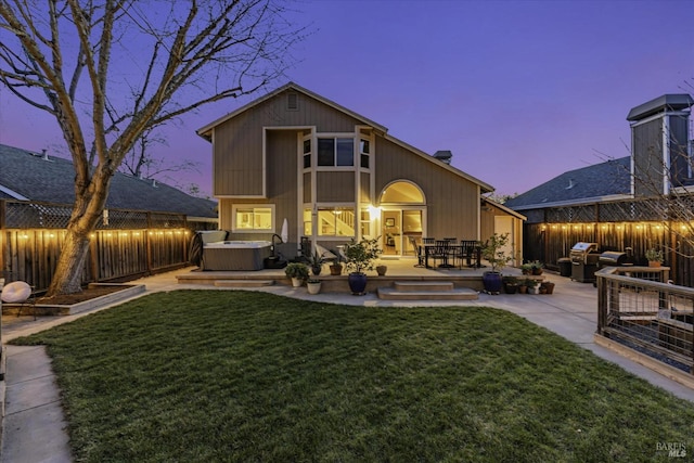 back house at dusk featuring an outbuilding, a yard, a hot tub, and a patio area