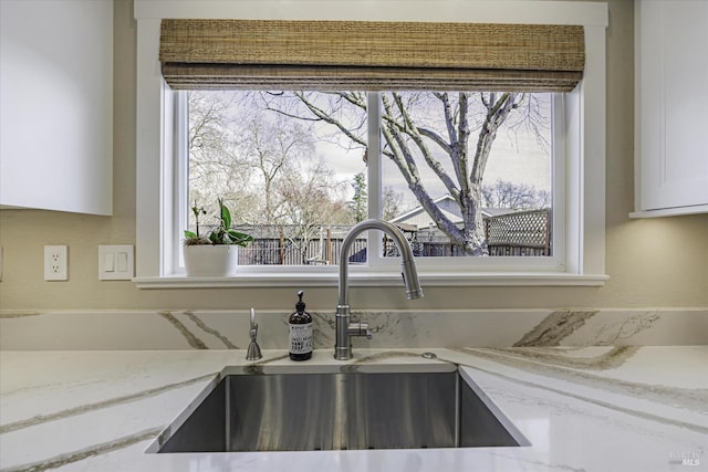 interior details featuring white cabinetry, sink, and light stone countertops