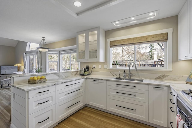 kitchen featuring sink, white cabinetry, stainless steel oven, light stone counters, and light hardwood / wood-style flooring