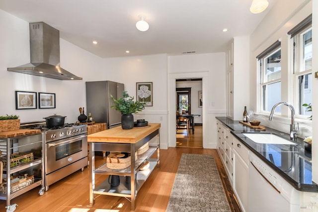 kitchen with visible vents, wall chimney exhaust hood, stainless steel appliances, white cabinetry, and a sink