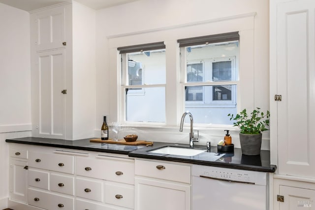 kitchen featuring dark countertops, white cabinets, dishwasher, and a sink