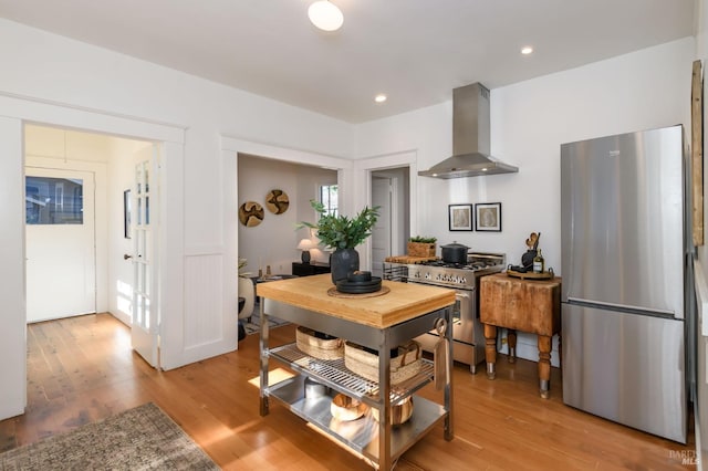 kitchen with stainless steel appliances, wall chimney range hood, light wood-style flooring, and recessed lighting