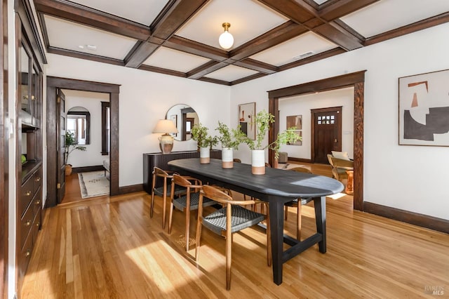 dining area featuring arched walkways, light wood-style flooring, coffered ceiling, baseboards, and beamed ceiling