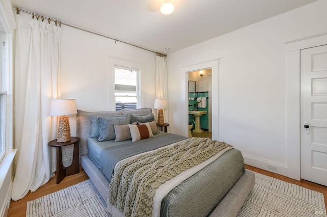 bedroom with ensuite bathroom, light wood-type flooring, and baseboards