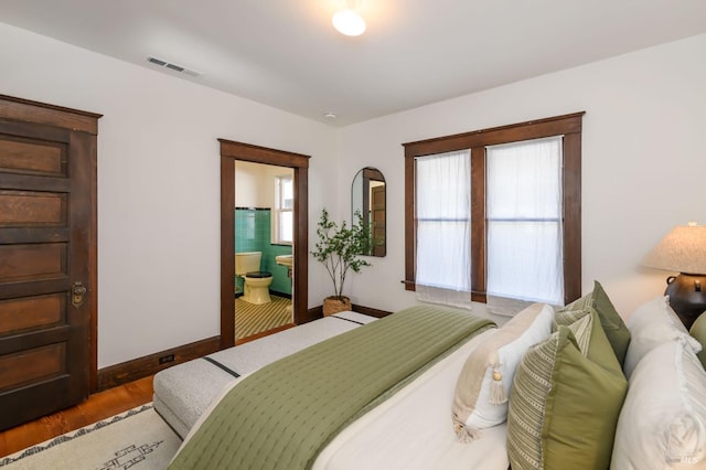 bedroom with visible vents, ensuite bath, baseboards, and wood finished floors