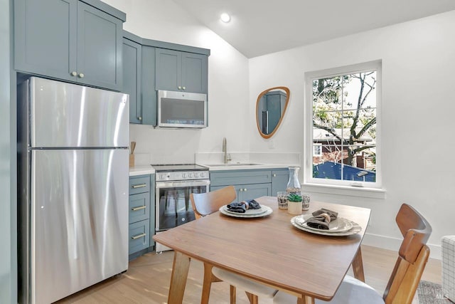 kitchen with sink, blue cabinetry, appliances with stainless steel finishes, light hardwood / wood-style floors, and vaulted ceiling