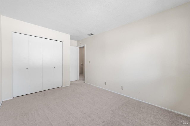 unfurnished bedroom with a closet, light carpet, and a textured ceiling