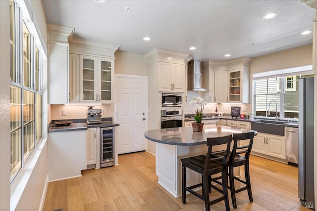 kitchen featuring wine cooler, sink, appliances with stainless steel finishes, wall chimney range hood, and white cabinets