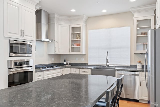 kitchen featuring sink, appliances with stainless steel finishes, white cabinetry, dark stone countertops, and wall chimney exhaust hood