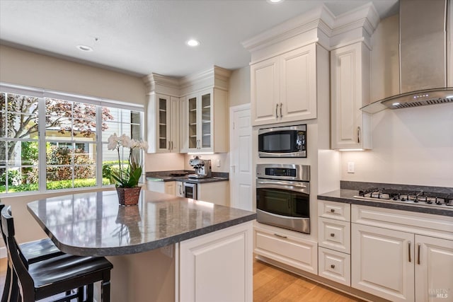 kitchen with a kitchen island, a breakfast bar, white cabinets, stainless steel appliances, and wall chimney range hood