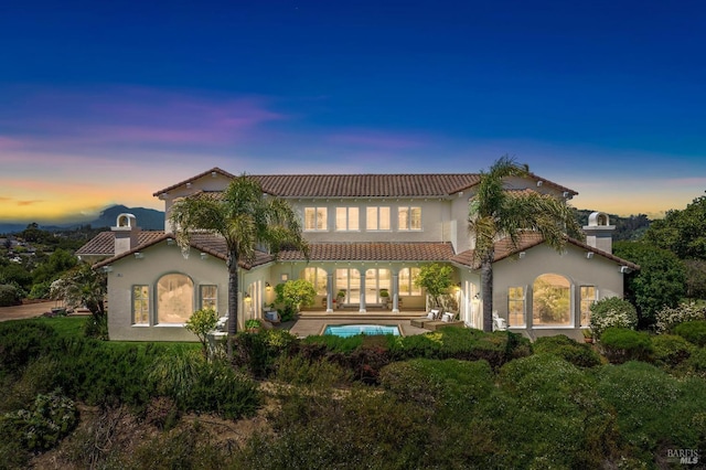 back of property at dusk featuring a patio area, a tile roof, an outdoor pool, and stucco siding