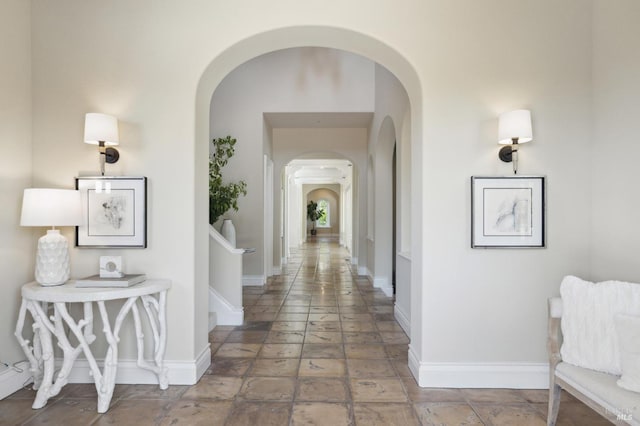 hall featuring baseboards, arched walkways, and stone tile flooring