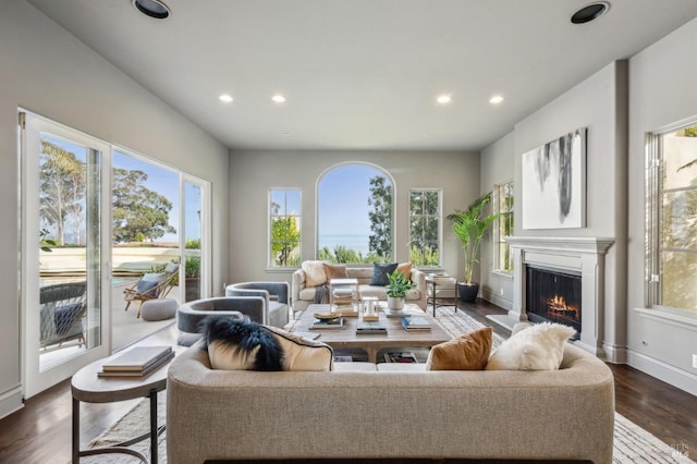 living room featuring a lit fireplace, baseboards, dark wood-type flooring, and recessed lighting